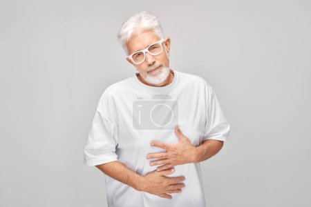 Téléchargez les photos : Portrait d'un homme mature souffrant de douleurs à l'estomac isolé sur fond de studio blanc. Concept de problèmes intestinaux et gastriques - en image libre de droit