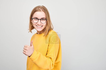 Photo for Portrait of young student girl smiling joyfully showing thumbs up gesture isolated on white studio background. Approves good choice, right decision - Royalty Free Image