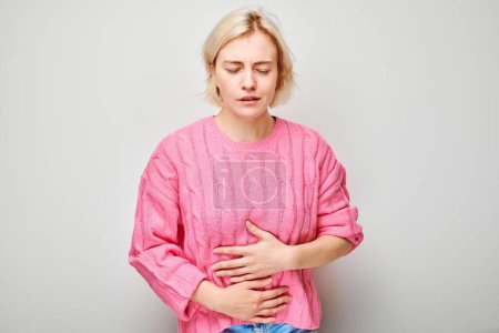 Foto de Retrato de una joven rubia que sufre de dolor de estómago aislado en el fondo blanco del estudio. Problemas intestinales y estomacales se contraen - Imagen libre de derechos