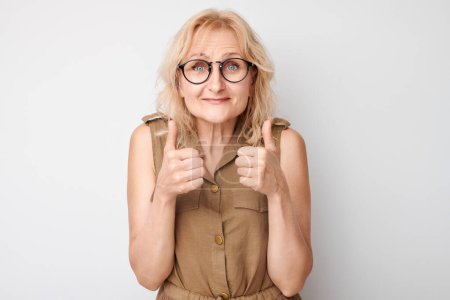 Photo for Portrait of mature woman with glasses smiling joyfully showing thumbs up gesture isolated on white studio background. Approves good choice, right decision - Royalty Free Image