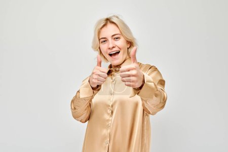 Téléchargez les photos : Portrait de jeune femme blonde en tenue décontractée souriant montrant joyeusement les pouces vers le haut geste isolé sur fond de studio blanc. Approuve le bon choix, la bonne décision - en image libre de droit