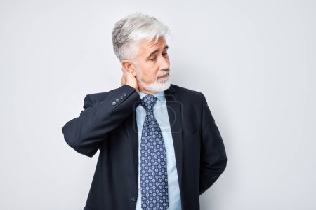 Photo for Portrait of mature gray-haired man suffering from pain, touching neck isolated on white studio background. Psychosomatics of stress, degenerative disease of spin - Royalty Free Image