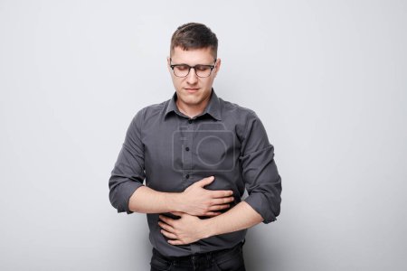 Photo for Portrait of young  suffering from stomach pain isolated on white studio background. Intestinal and stomach problems concept - Royalty Free Image