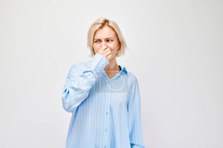 Foto de Retrato de una chica cubriéndose la nariz con una mano aislada sobre fondo blanco del estudio. Mala respiración, olor a sudor - Imagen libre de derechos