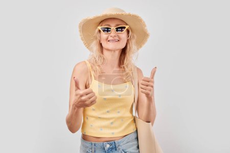 Foto de Retrato de una mujer madura con ropa de verano sonriendo alegremente mostrando el gesto de los pulgares hacia arriba aislado en el fondo blanco del estudio. Aprueba la buena elección, la decisión correcta - Imagen libre de derechos