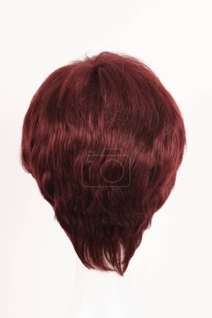 Téléchargez les photos : Perruque brune rouge naturelle sur tête de mannequin blanche. Cheveux foncés de longueur moyenne sur le porte-perruque en plastique isolé sur fond blanc - en image libre de droit