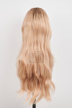 Photo for Natural looking blonde wig on white mannequin head. Long hair on the plastic wig holder isolated on white background, back vie - Royalty Free Image