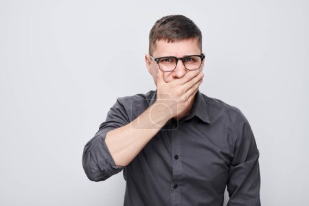 Photo for Portrait of man covering his mouth with hand isolated on white studio background. Bad breath concept, sweat smel - Royalty Free Image