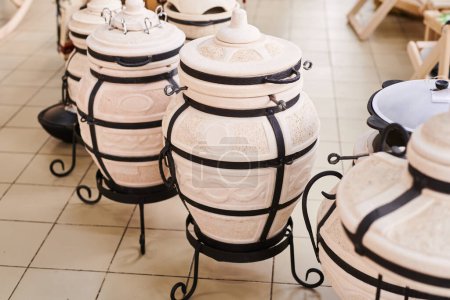 Téléchargez les photos : Four traditionnel en argile tandoor pour la fabrication de pains plats, grill et barbecue. Nouveaux ustensiles de cuisine en plein air sur la fenêtre du magasin - en image libre de droit