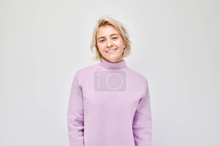 Photo for Portrait Caucasian young blond woman smiling joyfully isolated on white studio background. Happy girl in lilac sweater with glad face expressio - Royalty Free Image