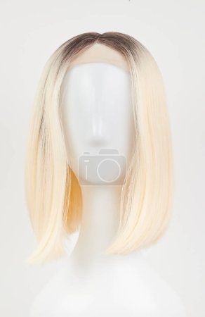 Photo for Natural looking blonde fair wig on white mannequin head. Middle length hair cut on the plastic wig holder isolated on white background, front vie - Royalty Free Image