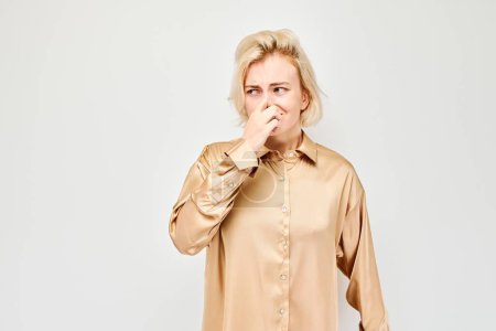 Téléchargez les photos : Portrait d'une fille couvrant son nez avec la main isolée sur fond de studio blanc. Concept de mauvaise haleine, odeur de sueur - en image libre de droit
