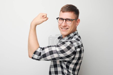 Foto de Retrato de un joven confiado mostrando bíceps, demostrando fuerza aislada sobre fondo blanco del estudio. Concepto ganador afortunado - Imagen libre de derechos