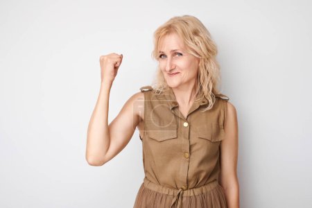 Foto de Retrato de mujer segura de 50 años mostrando bíceps, demostrando fuerza aislada sobre fondo blanco del estudio. Concepto ganador afortunado - Imagen libre de derechos
