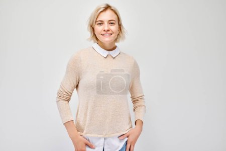 Téléchargez les photos : Portrait Femme blanche jeune blonde souriante joyeusement isolée sur fond de studio blanc. Fille heureuse en chemisier beige avec expression joyeuse du visage - en image libre de droit