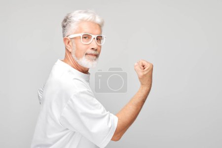 Téléchargez les photos : Portrait d'un homme confiant de 50 ans montrant des biceps, démontrant une force isolée sur fond de studio blanc. Concept de gagnant chanceux - en image libre de droit