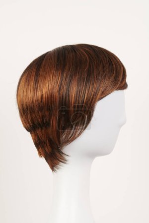 Photo for Natural looking dark brunet wig on white mannequin head. Short brown hair on the plastic wig holder isolated on white background, side vie - Royalty Free Image