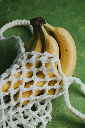 Téléchargez les photos : Gros plan de bananes dans un sac à ficelle sur fond vert - en image libre de droit