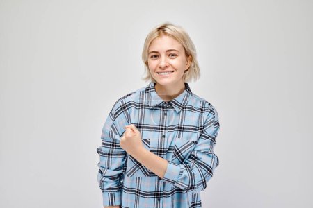 Téléchargez les photos : Portrait d'une jeune femme blonde confiante montrant des biceps, démontrant une force isolée sur fond de studio blanc. Gagnant chanceux concéder - en image libre de droit