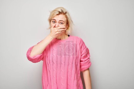 Téléchargez les photos : Portrait d'une fille couvrant sa bouche avec la main isolée sur fond de studio blanc. Concept de mauvaise haleine, odeur de sueur - en image libre de droit