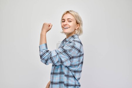 Téléchargez les photos : Portrait d'une jeune femme blonde confiante montrant des biceps, démontrant une force isolée sur fond de studio blanc. Gagnant chanceux concéder - en image libre de droit