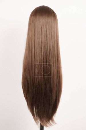 Photo for Natural looking dark brunet wig on white mannequin head. Long brown hair on the plastic wig holder isolated on white background, back vie - Royalty Free Image