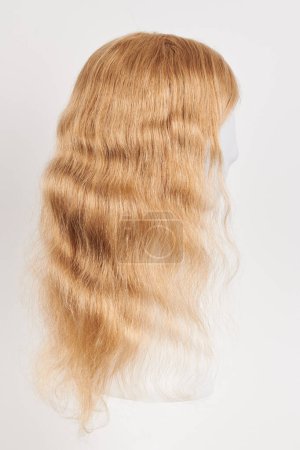 Photo for Natural looking blonde wig on white mannequin head. Long hair on the plastic wig holder isolated on white background, side vie - Royalty Free Image