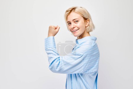 Photo for Portrait of confident young blonde woman showing biceps, demonstrating strength isolated on white studio background. Lucky winner concep - Royalty Free Image