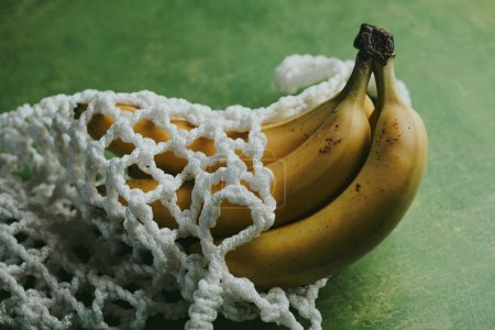Photo for Close-up of bananas in a string bag on a green background - Royalty Free Image