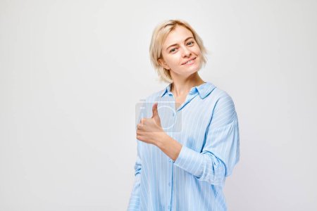 Photo for Portrait of young blond woman in casual clothing smiling joyfully showing thumbs up gesture isolated on white studio background. Approves good choice, right decisio - Royalty Free Image