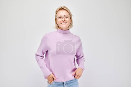 Photo for Portrait Caucasian young blond woman smiling joyfully isolated on white studio background. Happy girl in lilac sweater and glasses with glad face expression - Royalty Free Image