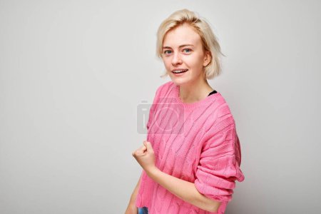 Foto de Retrato de una joven rubia confiada mostrando bíceps, demostrando fuerza aislada sobre fondo blanco del estudio. Concepto ganador afortunado - Imagen libre de derechos