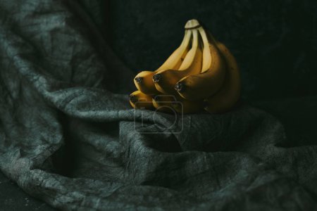 Téléchargez les photos : Gros plan d'un bouquet de bananes sur un fond de tissu sombre - en image libre de droit