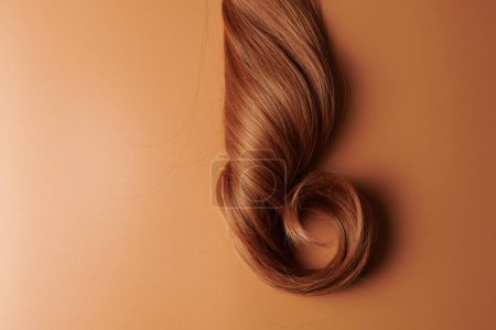 Foto de Cabello brillante de aspecto natural, mechón de color marrón morena rizos aislados sobre fondo naranja - Imagen libre de derechos