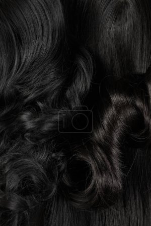 Foto de Cabello brillante de aspecto natural, racimo de colores morenos oscuros rizos y pelucas aisladas sobre fondo negro - Imagen libre de derechos