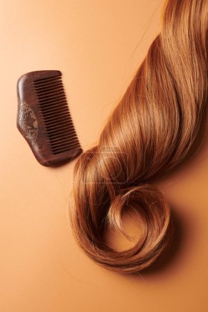 Téléchargez les photos : Boucles de cheveux bruns et un peigne en bois sur un fond orange, soins des cheveux, concept de salon de beauté - en image libre de droit