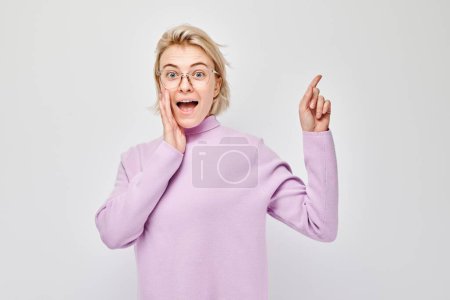 Foto de Mujer rubia joven en casual señalando a un lado el dedo, demostrando el espacio vacío para el producto o el texto aislado en el fondo del estudio blanco - Imagen libre de derechos