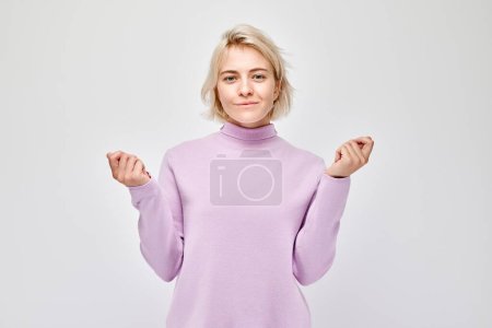 Foto de Mujer rubia joven en casual sosteniendo algo en la mano, demostrando espacio vacío para producto o texto aislado en fondo de estudio blanco - Imagen libre de derechos