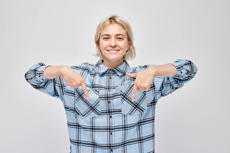 Téléchargez les photos : Jeune femme blonde au doigt pointant vers le bas, démontrant un espace vide pour le produit ou le texte isolé sur fond de studio blanc - en image libre de droit