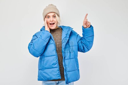 Photo for Young woman in blue winter jacket pointing aside finger, demonstrating empty space for product or text isolated on white studio backgroun - Royalty Free Image