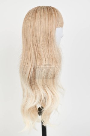 Téléchargez les photos : Perruque blonde naturelle sur tête de mannequin blanche. Cheveux longs sur le support de perruque en plastique isolé sur fond blanc, vie latérale - en image libre de droit