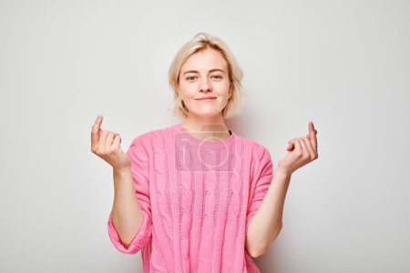 Téléchargez les photos : Jeune femme blonde en pull rose tenant quelque chose en main, démontrant un espace vide pour le produit ou le texte isolé sur fond de studio blanc - en image libre de droit