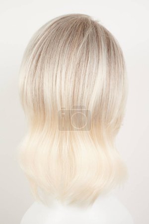 Photo for Natural looking blonde fair wig on white mannequin head. Middle length hair cut on the plastic wig holder isolated on white background, back view - Royalty Free Image