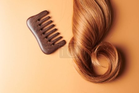 Foto de Rizos de cabello castaño y un peine de madera sobre un fondo naranja, cuidado del cabello, concepto de salón de belleza - Imagen libre de derechos