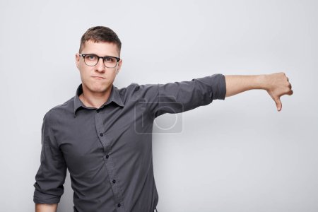 Photo for Portrait of man in shirt and glasses showing thumbs down isolated on white studio background. Dislike, wrong choice, negative evaluation concep - Royalty Free Image