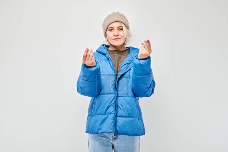 Téléchargez les photos : Jeune femme veste d'hiver bleue tenant quelque chose en main, démontrant un espace vide pour le produit ou le texte isolé sur fond de studio blanc - en image libre de droit
