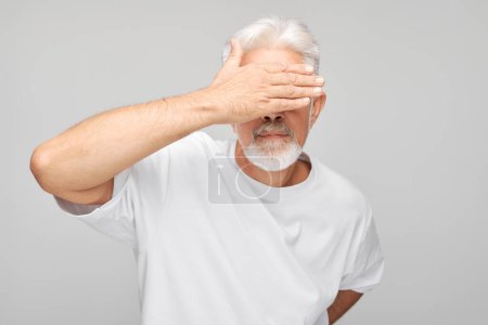 Téléchargez les photos : Portrait d'homme âgé couvrant les yeux à la main isolé sur fond de studio blanc - en image libre de droit