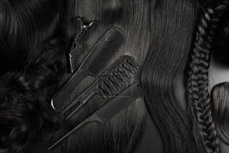 Téléchargez les photos : Outils de coiffure close-up isolé sur fond noir. Boucles de cheveux bruns foncés et un ensemble de peignes, clips, épingles à cheveux, concept de salon de beauté pour cheveux - en image libre de droit