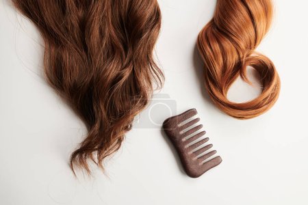 Photo for Curls of brown hair and a wooden comb on a white background, hair care, beauty salon concept - Royalty Free Image