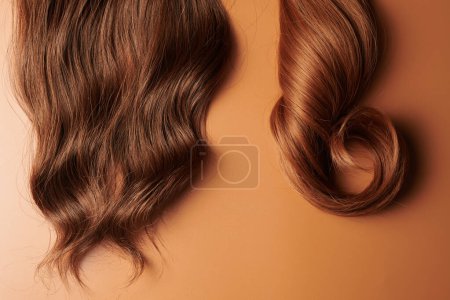 Téléchargez les photos : Cheveux naturels brillants, mèche de couleurs brunes brunes brunes boucles isolées sur fond orange - en image libre de droit
